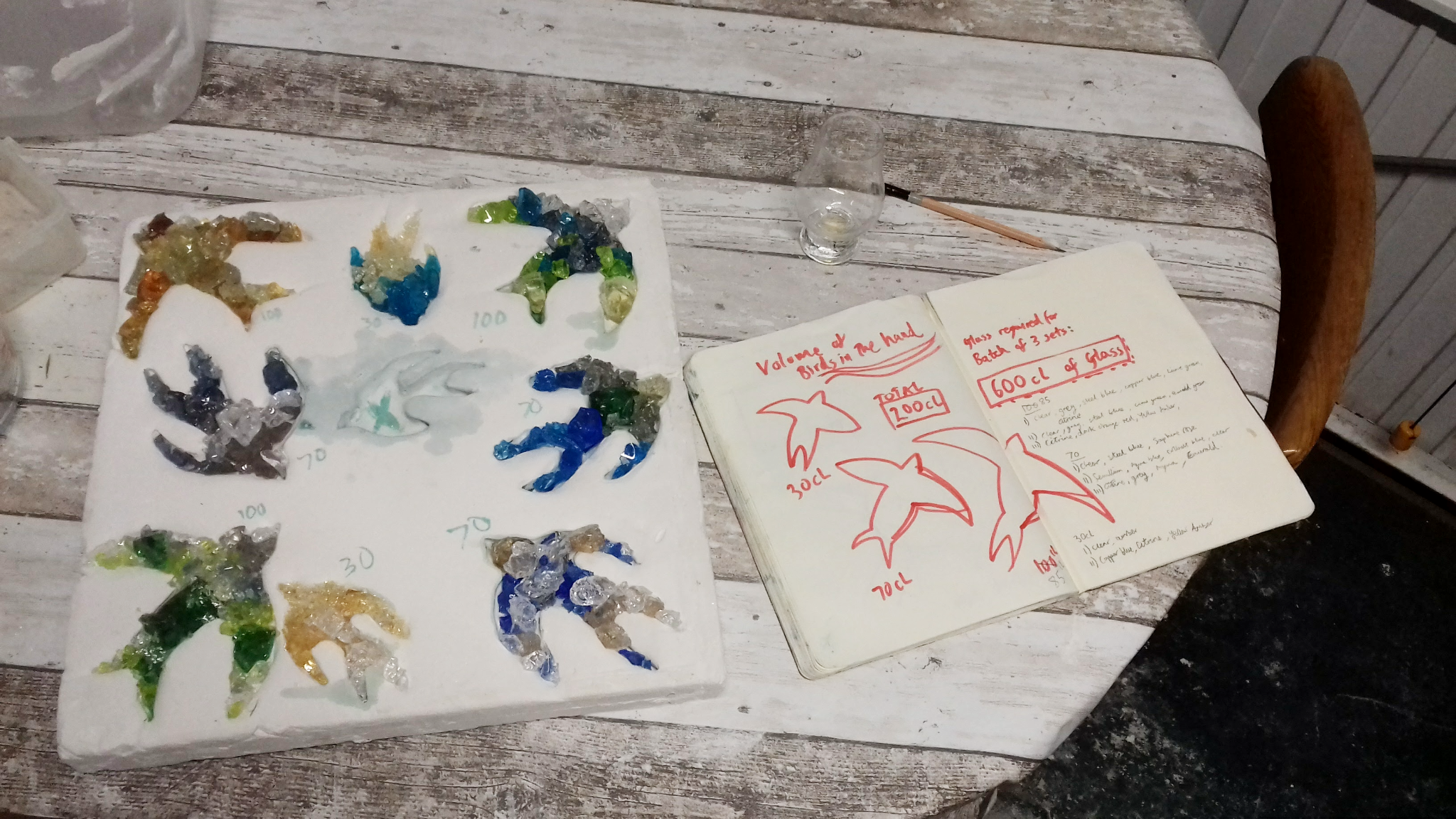 Glass crystals arranged as swift forms beside process notes recording the quantities required for kiln forming